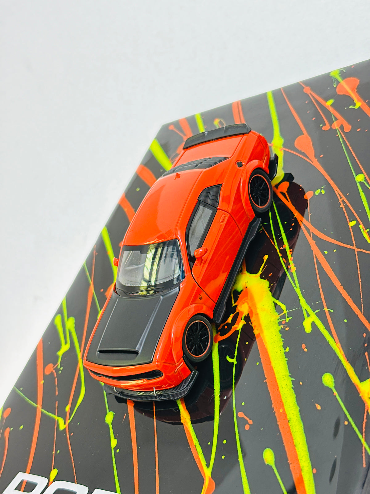 Orange Dodge miniature car on black resin display frame with neon splatter design