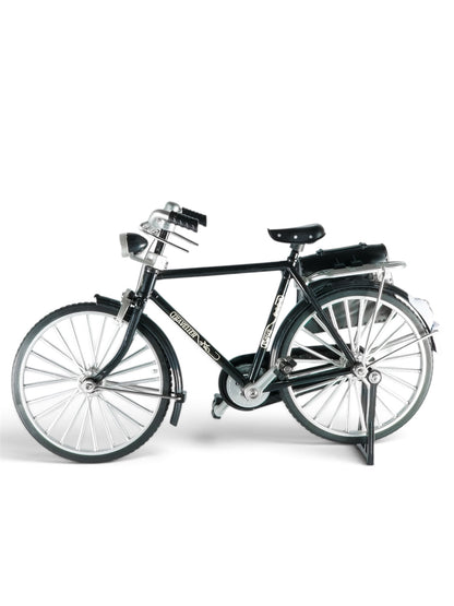 Descriptive: Front-three-quarter view of a miniature black classic city bike with silver mechanical details, black seat, and a dark pannier bag attached to the rear rack.